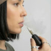 Close-up side view of a woman exhaling vapour while holding a G Pen 510 OG