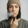 Woman using a G Pen 510 OG battery with a cartridge and exhaling vapour